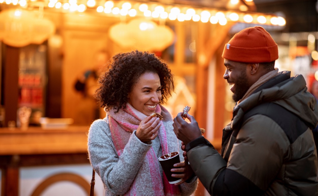 2 people enjoy cups of cocoa at an outdoor holiday market